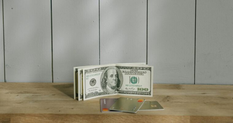 Three 100-dollar bills and credit cards on a wooden desk.