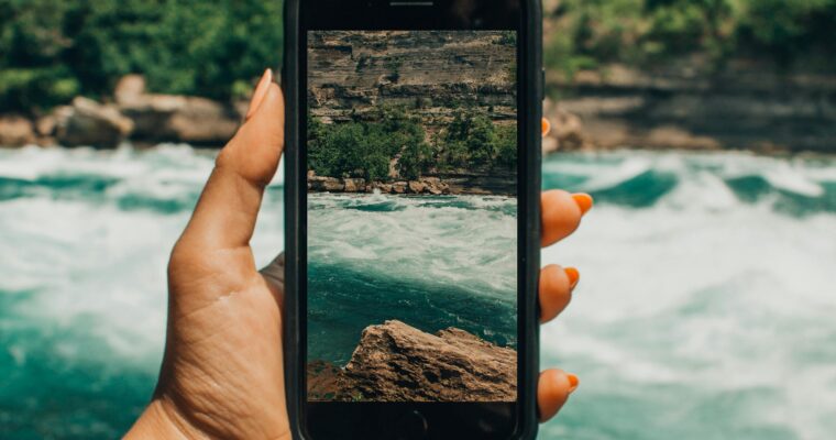 A woman's hand holding an iPhone and taking a picture of a river.